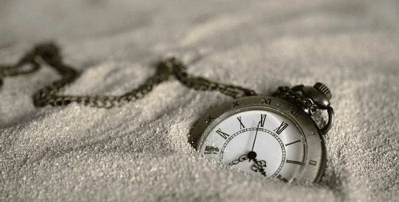 a beige colour pocket watch partially buried on sand