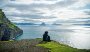 a person sitting at the edge of a cliff facing towards the sea in daylight