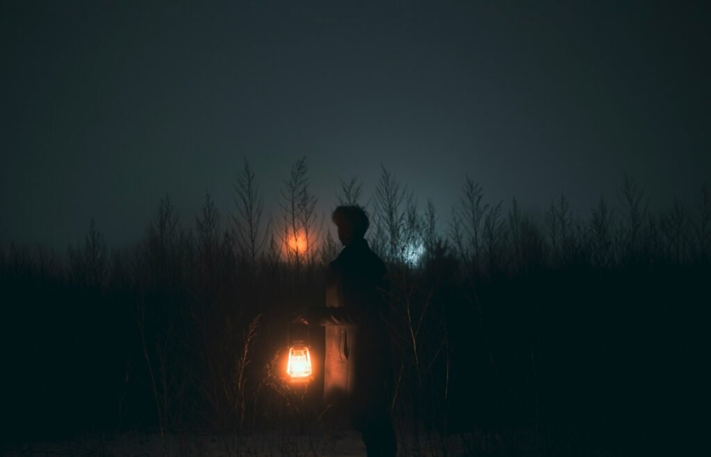 alone boy at night in a bushes carrying a lantern with lights reflecting from the horizon