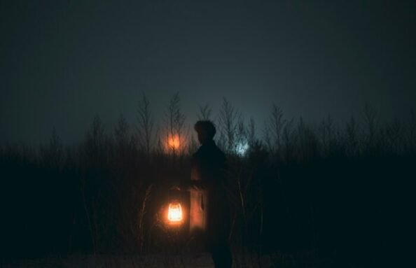 alone boy at night in a bushes carrying a lantern with lights reflecting from the horizon